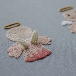 Detail shot focusing on the back of an embroidered angel, highlighting the spiral stitch on its head and its small white wings.