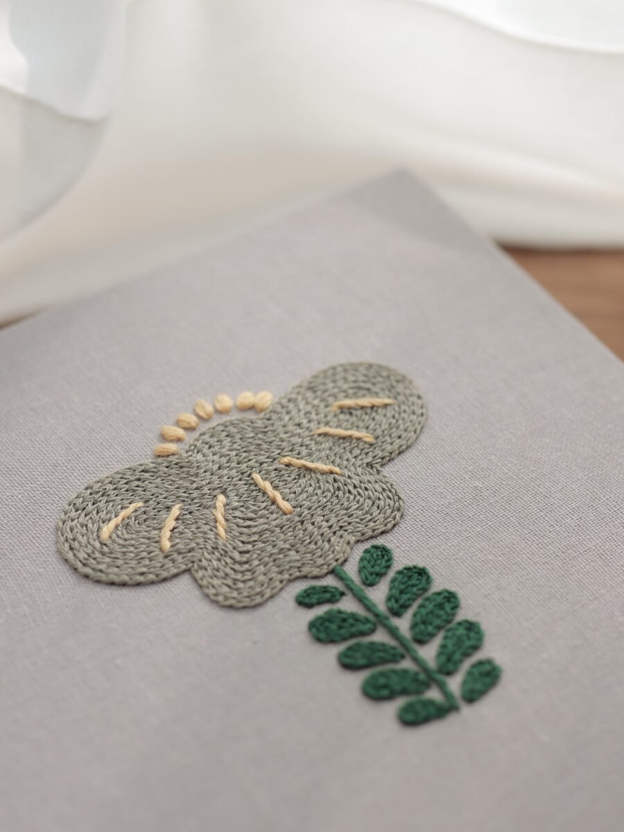 Angled detail shot of an embroidered panel from "Botanical Observation No. 5," highlighting the raised texture of the stitching against a soft, naturally lit background.
