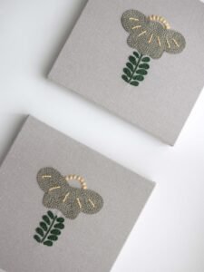 Overhead view of two panels from the "Botanical Observation No. 5" triptych, showing the repeated embroidered floral motif on grey canvas.