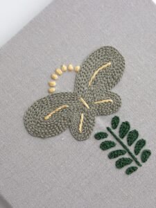Close-up of a single panel from "Botanical Observation No. 5," showing the detailed texture of the grey chain stitch flower and green satin stitch leaves on grey canvas.