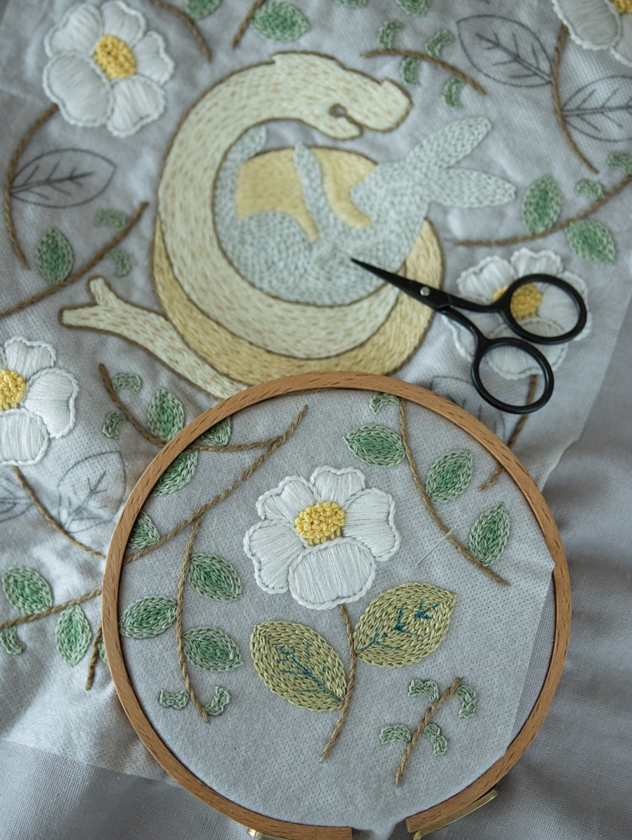 In-progress detail of 'The Year of Snake' embroidery, with the wooden hoop in the foreground and visible pattern lines on the fabric.