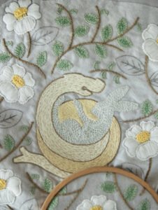  Work-in-progress shot of 'The Year of Snake' embroidery, with a hoop showing a detailed white flower and a pair of black embroidery scissors resting on the fabric.