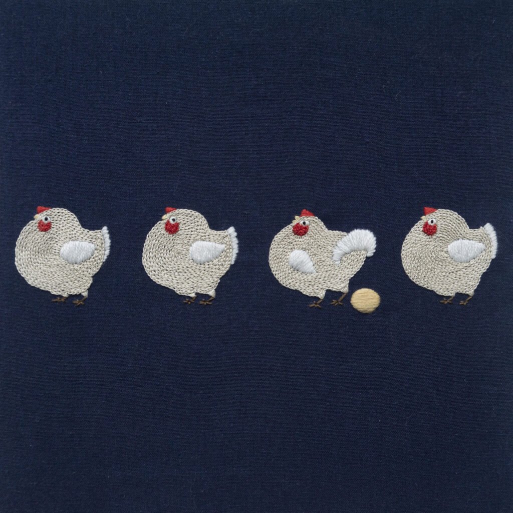 Hand embroidery of four plump, off-white chickens on navy blue fabric; the third chicken stands proudly beside a golden egg it has just laid. Image Title (in WordPress Media Library): Embroidery Art - A Maverick Chicken