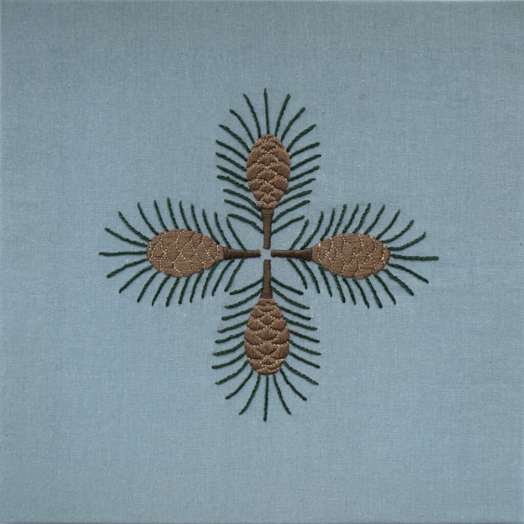 A Whisper Across Time: For the Art That Waits for Its Listener Hand embroidery titled "Pine," featuring a symmetrical design of four pinecones and needles on a dusty blue fabric.