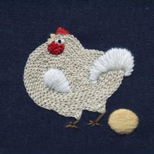 Detail shot from the embroidery artwork 'A Maverick Chicken,' focusing on the individual chicken and its golden egg. The intricate threadwork highlights the plump texture of the chicken against the dark background.