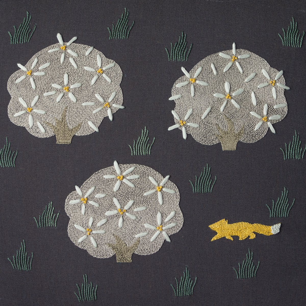 Woodland Fox and Trees Hand Embroidery Hand embroidery of a yellow fox walking past three stylized flowering trees on dark grey fabric.