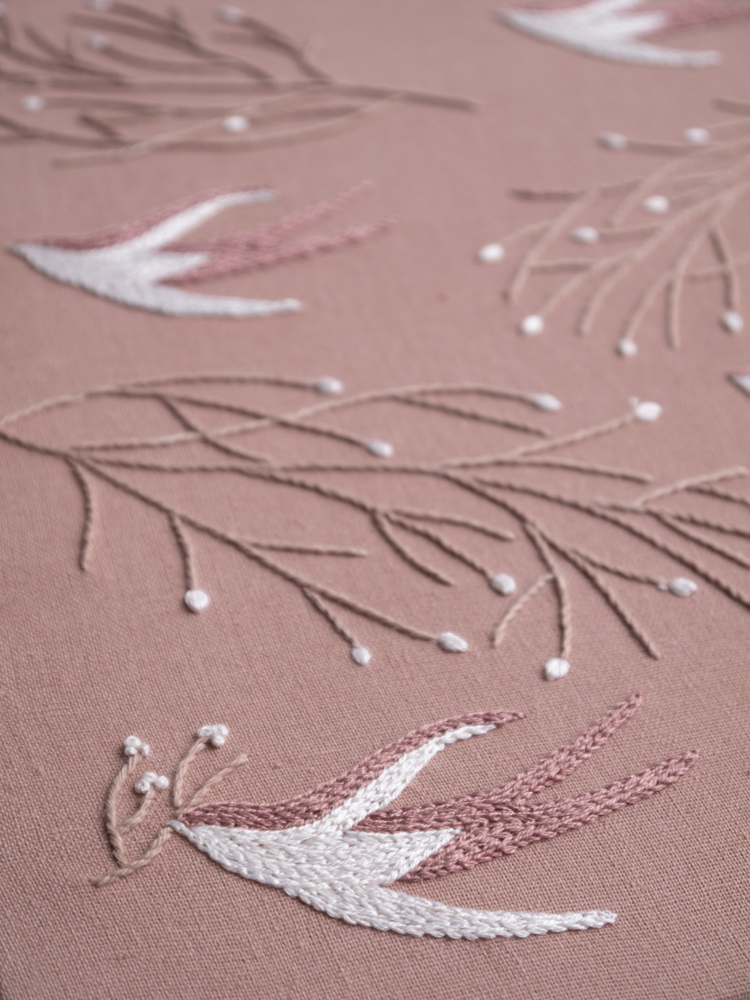 Close-up of a modern embroidery pattern featuring a stylized swallow and branches.