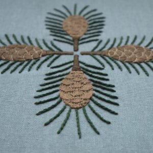Detail shot of the "Pine" embroidery, focusing on the texture of the satin-stitched pinecones and straight-stitched needles on the blue fabric.