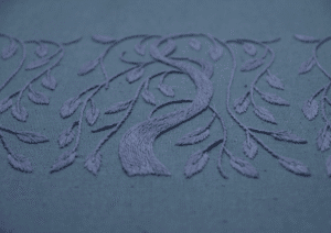 A detailed close-up of the 'Willow' embroidery, highlighting the satin stitch texture of the tree trunk and leaves in periwinkle thread on blue linen.