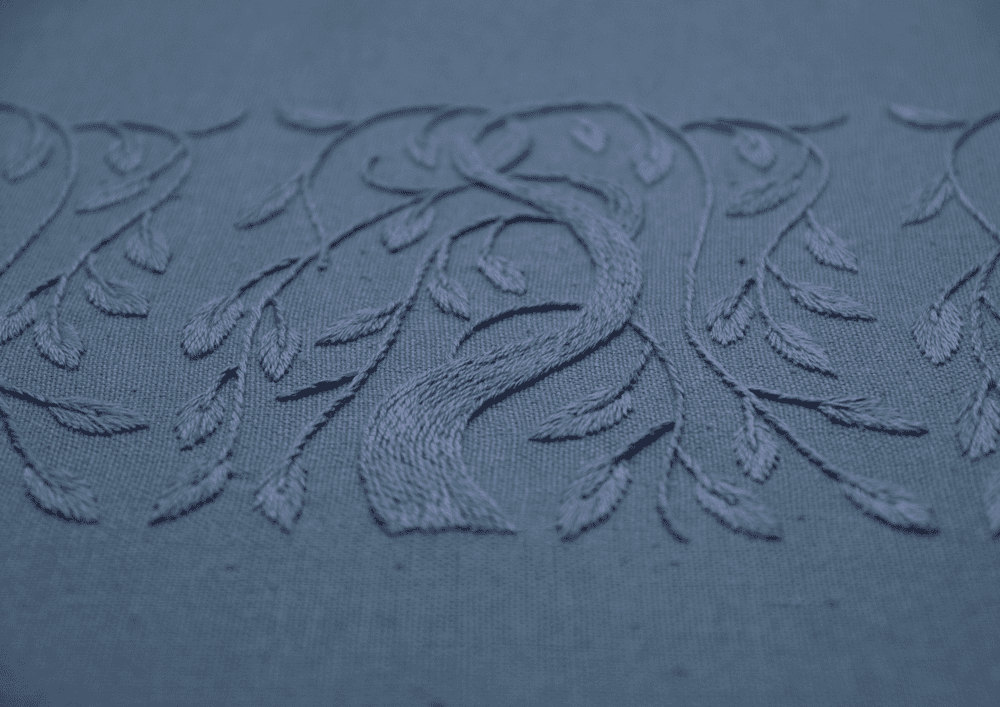 A detailed close-up of the 'Willow' embroidery, highlighting the satin stitch texture of the tree trunk and leaves in periwinkle thread on blue linen.