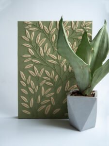 Finished botanical leaf embroidery on a sage green canvas, displayed next to a live snake plant in a geometric concrete pot.