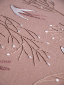 Detailed macro shot of hand embroidery, highlighting the texture of a outline-stitched branches and chain stitch bird.