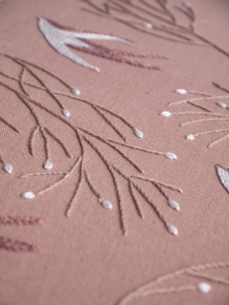 Detailed macro shot of hand embroidery, highlighting the texture of a outline-stitched branches and chain stitch bird.