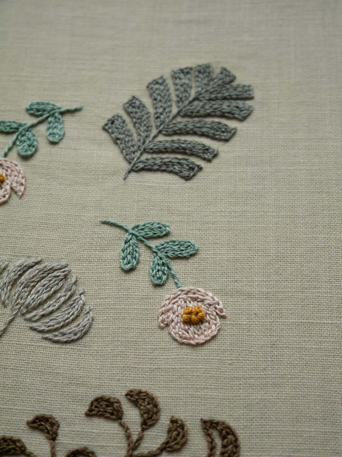 A close-up of hand-embroidered motifs by lissyluo, showing the detailed stitching of a pink flower and a grey monstera leaf.