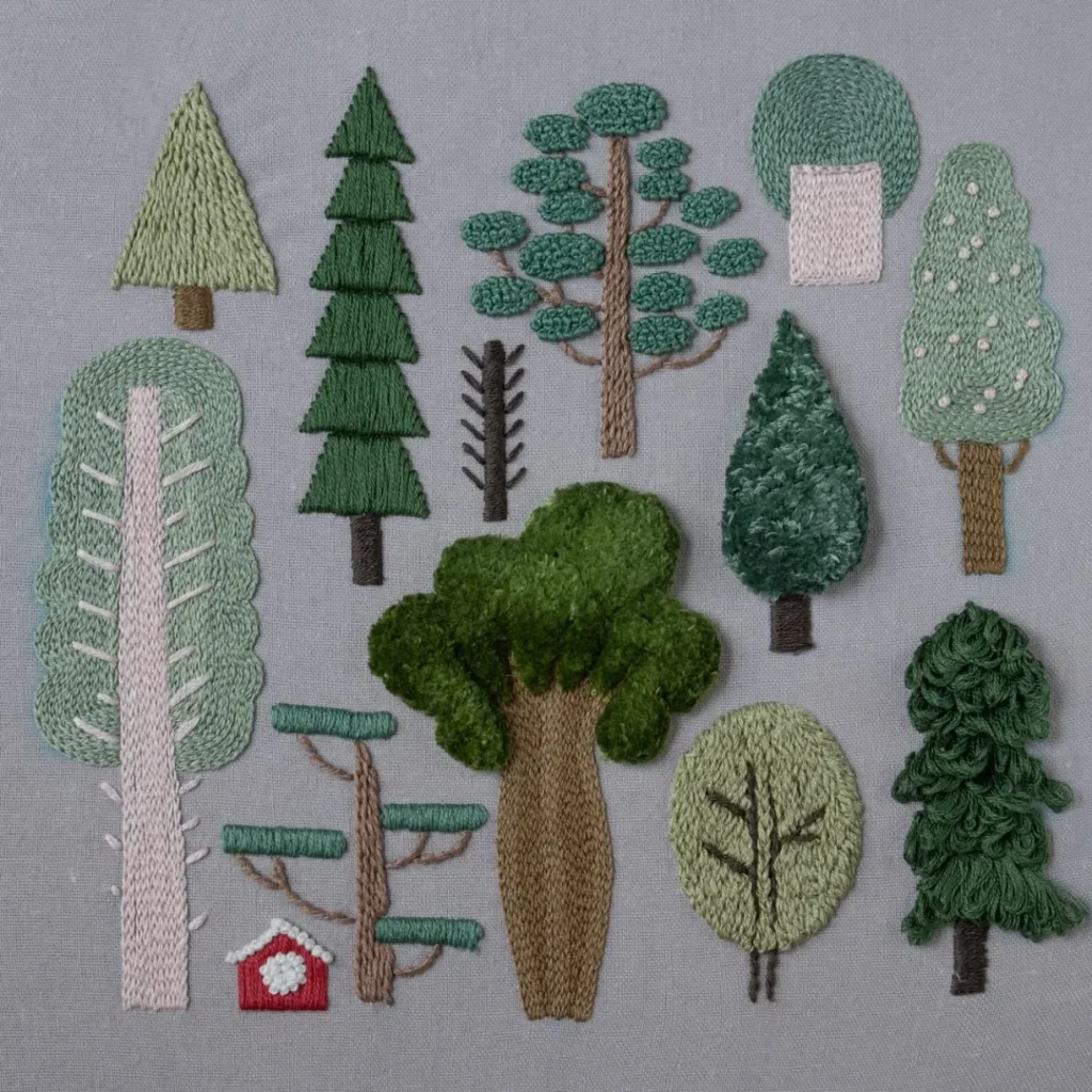 A hand embroidery piece named "Forest," showcasing various stylized trees stitched in green and brown thread on grey fabric.