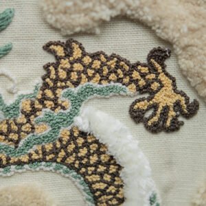 A close-up of the hand-embroidered dragon's body, highlighting the textured punch needle scales in brown and yellow and a detailed claw.
