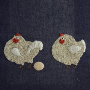 `Hand embroidery of two plump chickens on navy blue fabric; one stands beside a golden egg while the other looks on.`