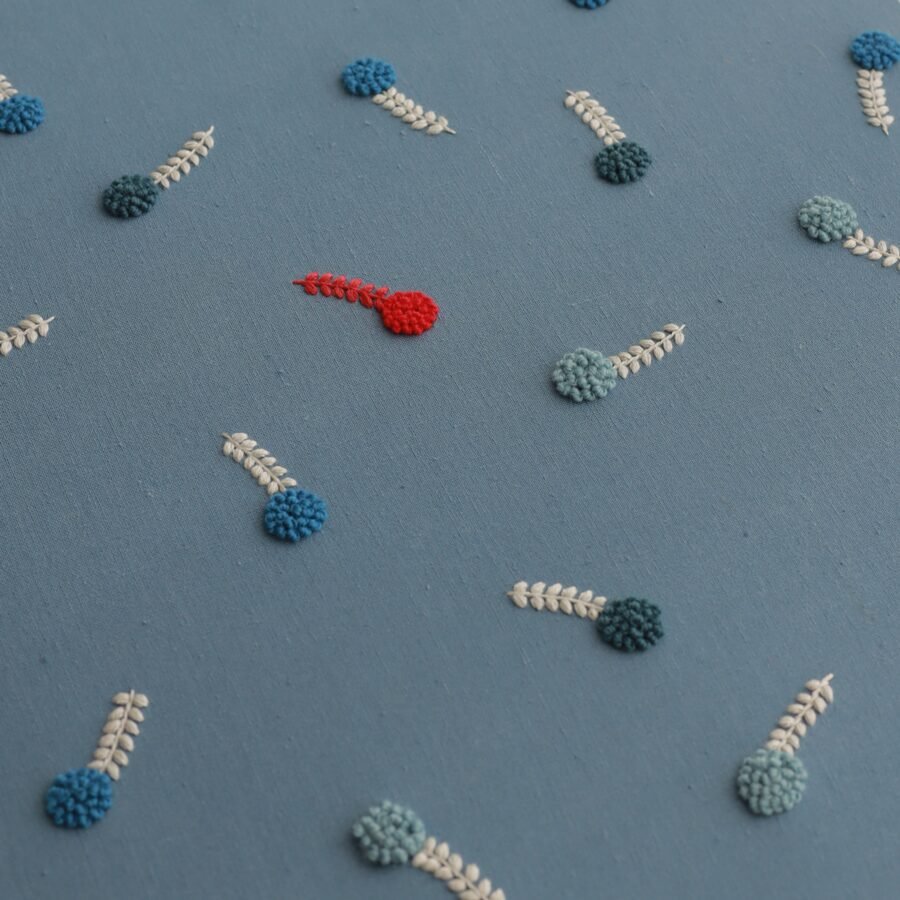 A close, angled shot of the embroidery, focusing on the arrangement of the stylized blue and red flowers on a blue linen background.