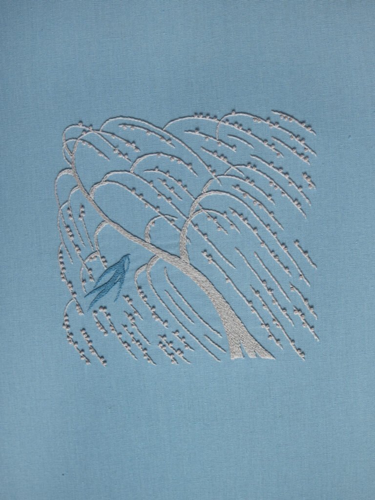 Hand embroidery of a windblown weeping willow and a blue swallow, created with white outline stitches and French knots on light blue fabric.