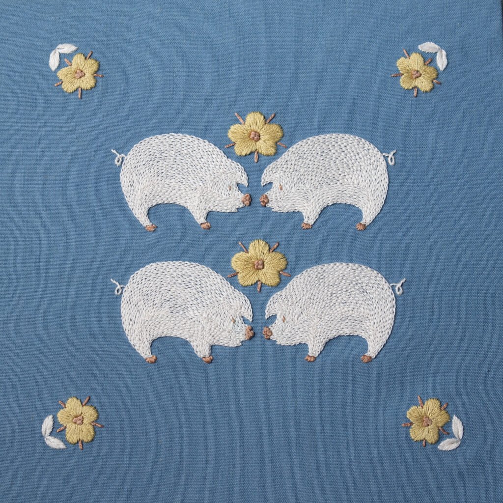 Symmetrical hand embroidery of four white pigs and yellow flowers on a blue canvas. The artwork, 'Piglet and Huahua,' shows two pairs of pigs facing each other.