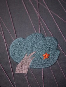  Extreme close-up on the embroidered tree, highlighting the texture of the fill stitch and the single orange lazy daisy stitch flower.