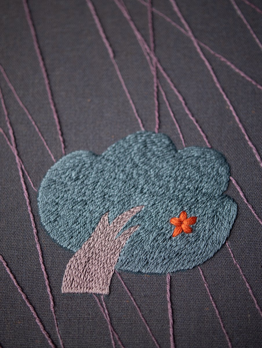  Extreme close-up on the embroidered tree, highlighting the texture of the fill stitch and the single orange lazy daisy stitch flower.
