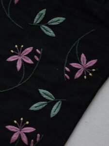 Angled close-up of the botanical embroidery, showing the texture of the pink and green thread on the black canvas fabric.