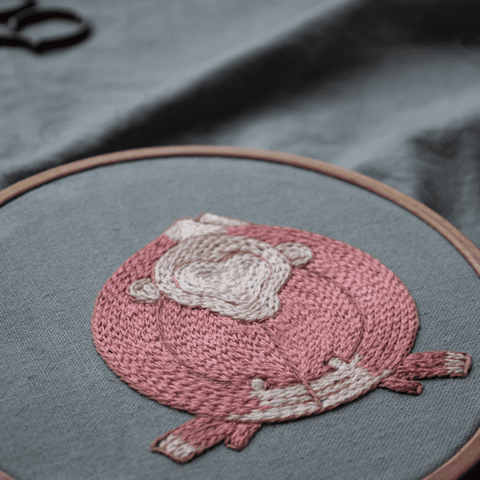 Close-up detail of a pink monkey figure from the 'Embracing Loneliness' artwork, highlighting the texture of the satin stitch embroidery in the hoop