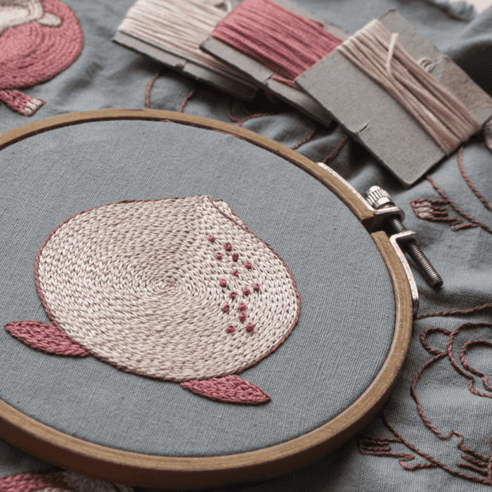 A detailed close-up of the central peach motif from 'Embracing Loneliness,' showcasing the spiral satin stitch and pink French knots within the embroidery hoop.