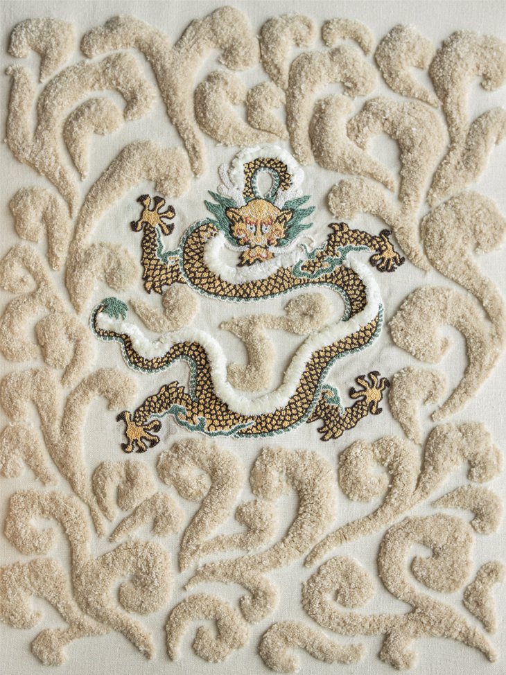 A hand-embroidered Chinese dragon with gold and black scales, surrounded by raised, beige tufted clouds on an off-white canvas.