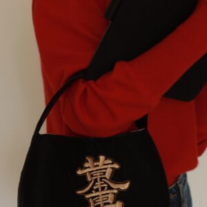 Black shoulder bag with gold 'Golden Prosperity' embroidery, styled with a red sweater and jeans.