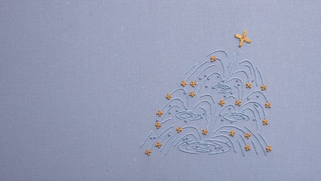 Detail of an abstract fountain embroidery by lissyluo. Light blue thread creates swirling water patterns on pale blue fabric, accented with golden-yellow floral stitches.