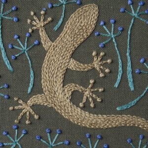 Detailed hand embroidery of a beige gecko on dark green fabric, surrounded by stylized blue flowers.